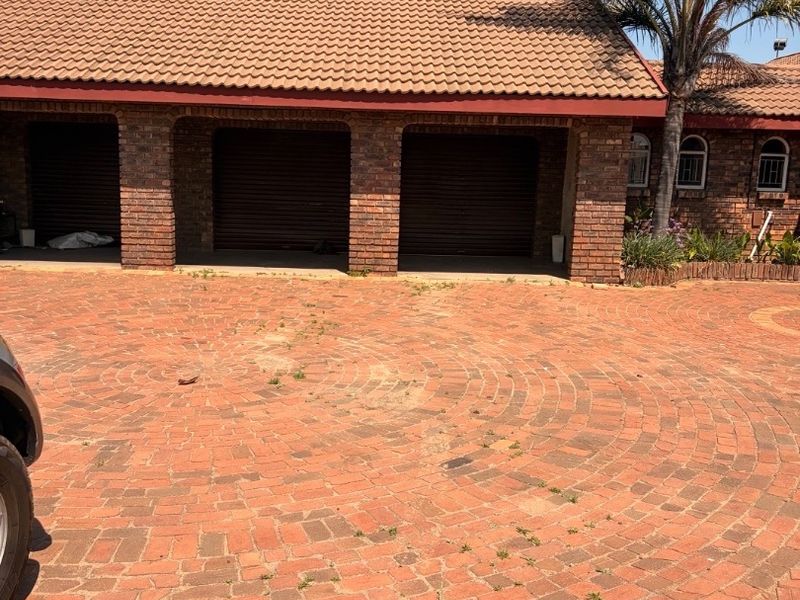 Front view of a property featuring a triple garage with brick facade, tiled roof, and a circular brick paved driveway.