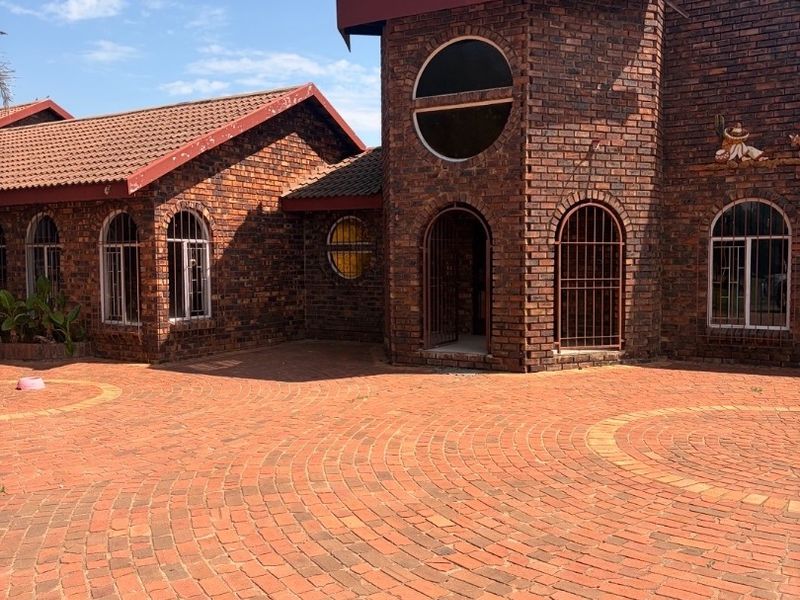 Front elevation of a face brick house featuring arched windows, a circular architectural detail, and an extensive brick-paved driveway.