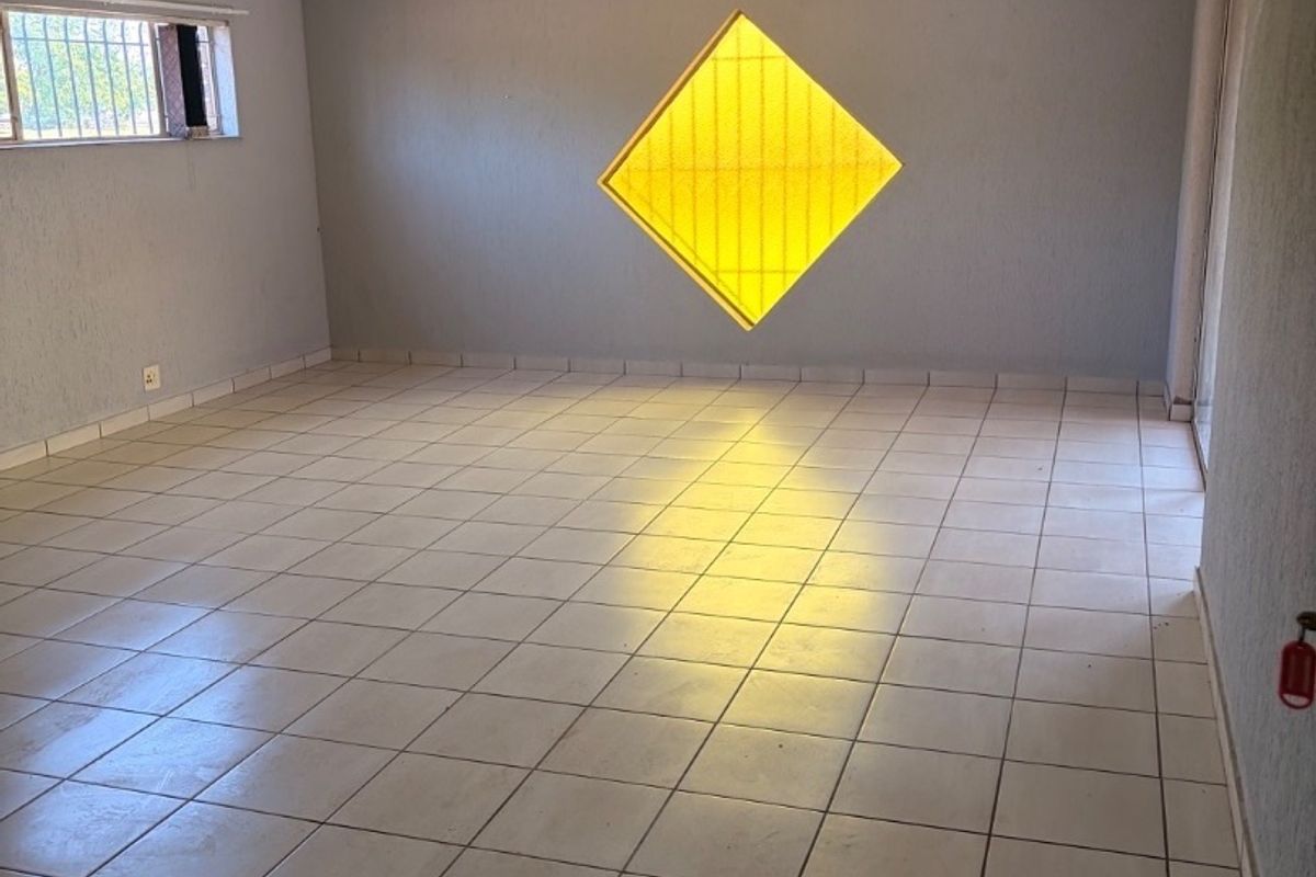An empty living area featuring ceramic floor tiles and a unique diamond-shaped feature window, offering a blank canvas for interior design.