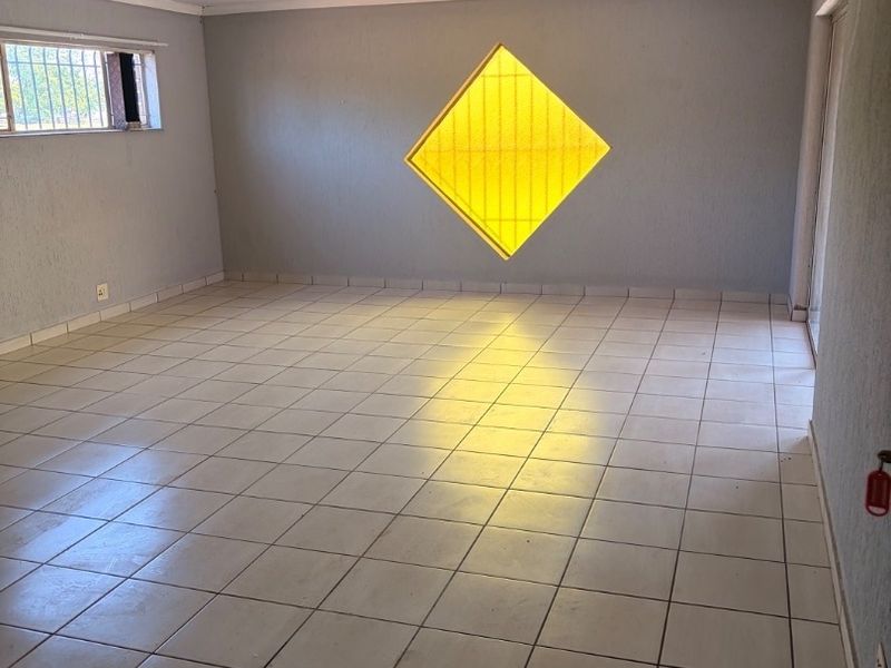 An empty living area featuring ceramic floor tiles and a unique diamond-shaped feature window, offering a blank canvas for interior design.