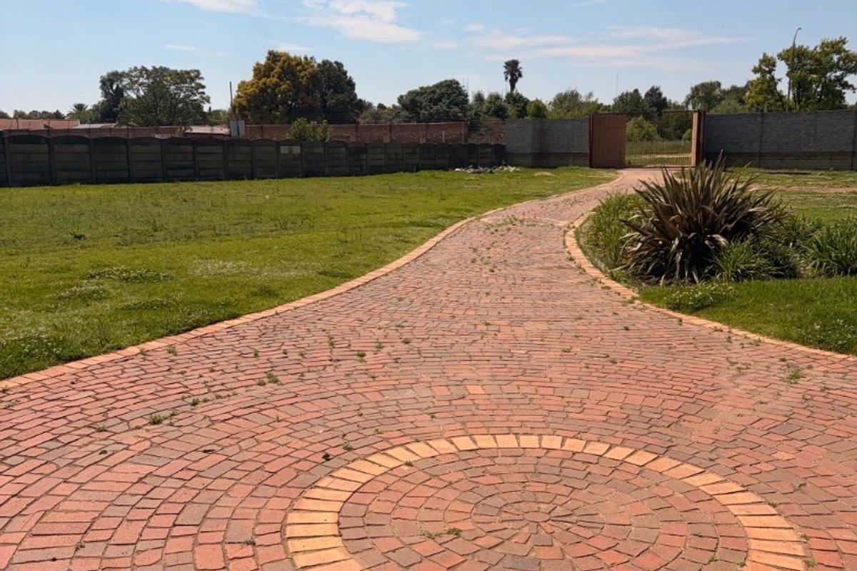 A spacious garden area featuring a decorative circular brick paved driveway and perimeter boundary walls.