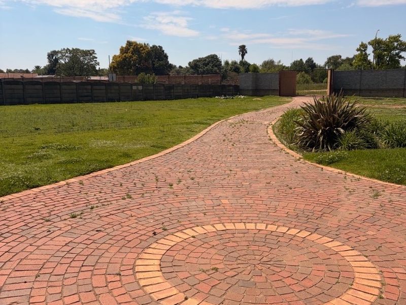 A spacious garden area featuring a decorative circular brick paved driveway and perimeter boundary walls.