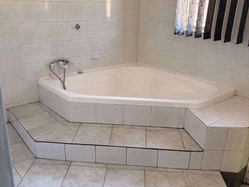 A bathroom featuring a raised corner bathtub with tiled steps and wall tiling, requiring some maintenance and cosmetic updates.