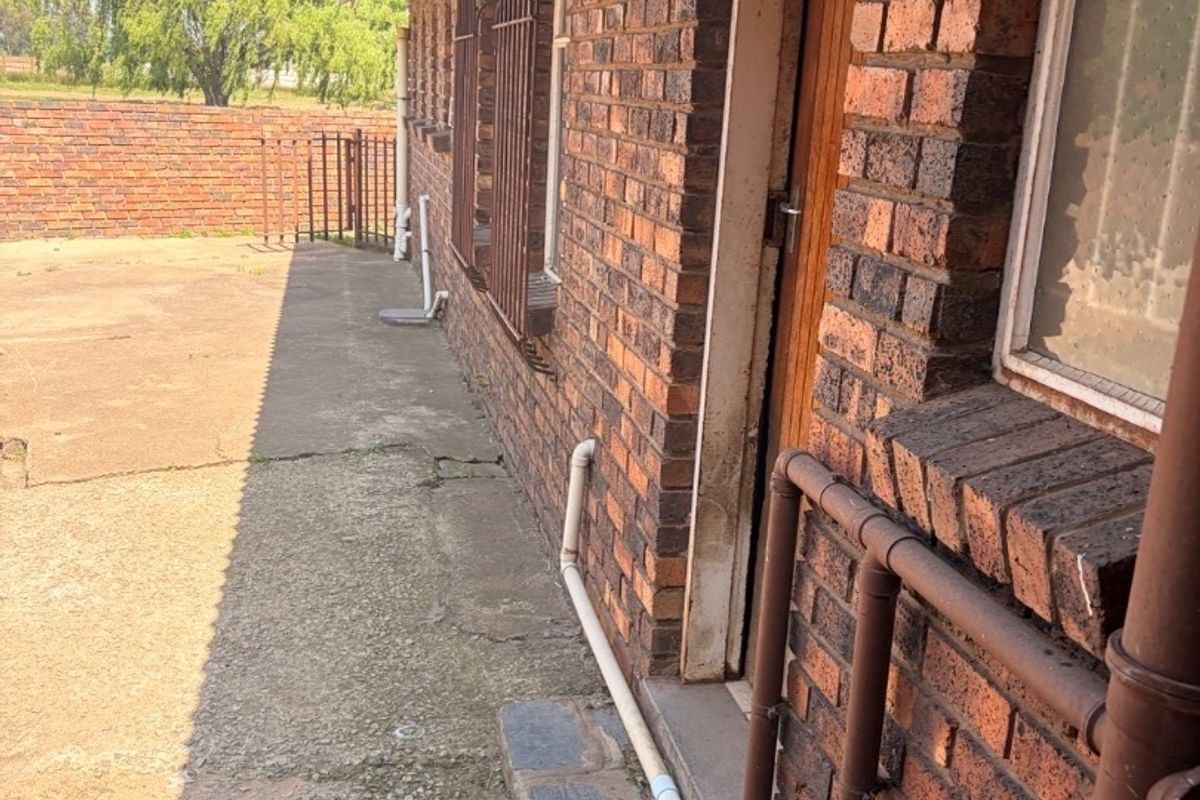 Rear exterior view of the property featuring exposed brick walls, concrete paving, and security bars on windows.