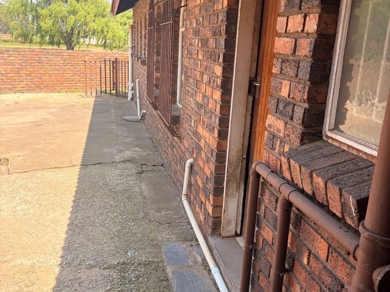 Rear exterior view of the property featuring exposed brick walls, concrete paving, and security bars on windows.