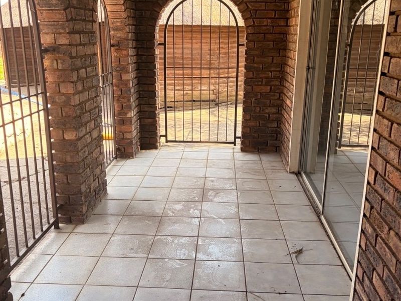 A covered patio area featuring exposed brick arches, tiled flooring, and secure metal gates, providing direct access to the home through sliding glass doors.