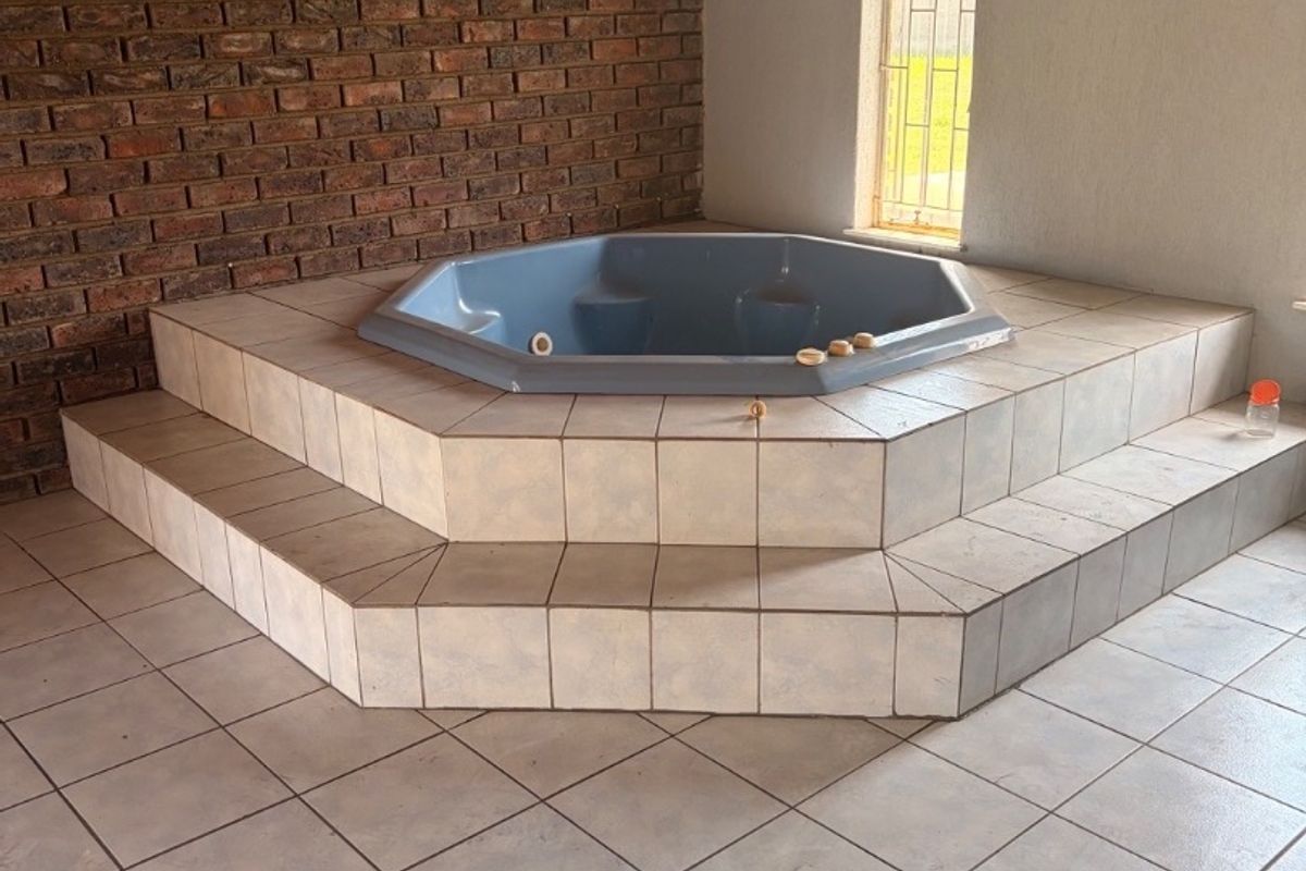 Spacious bathroom featuring a built-in sunken bathtub on a tiled platform, accented by an exposed brick wall and arched window.