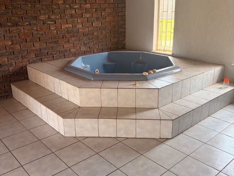 Spacious bathroom featuring a built-in sunken bathtub on a tiled platform, accented by an exposed brick wall and arched window.