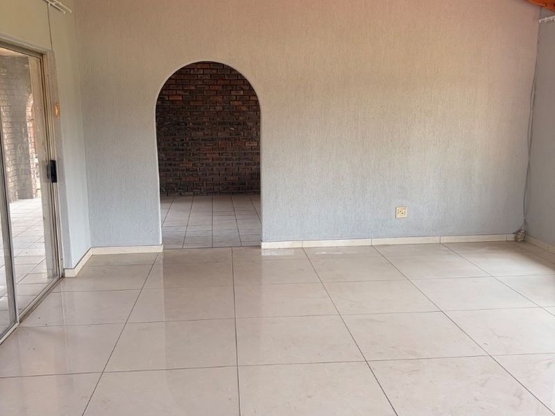 Spacious living area featuring high exposed timber rafter ceilings, neutral tiled flooring, and an arched doorway leading to an exposed brick space.