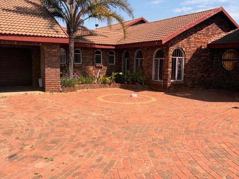 Front exterior view of a face brick house featuring a circular paved driveway, arched windows, and a tiled roof.