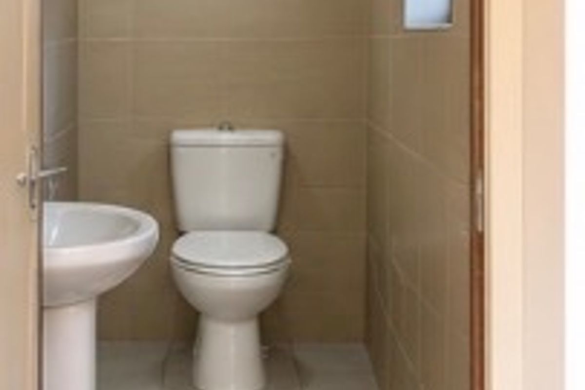 A clean and functional guest bathroom featuring a pedestal washbasin, toilet, and neutral ceramic tiling throughout.