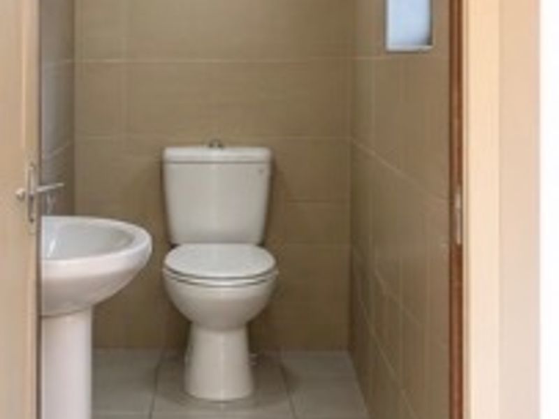 A clean and functional guest bathroom featuring a pedestal washbasin, toilet, and neutral ceramic tiling throughout.