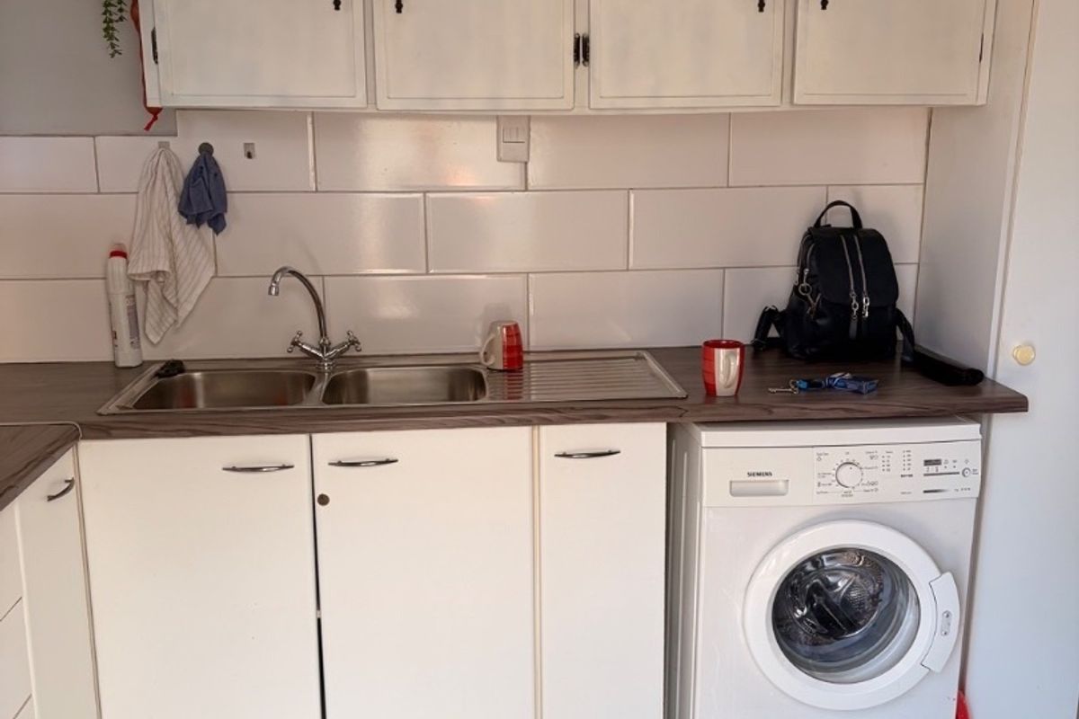 A functional laundry area featuring built-in white cabinetry, a stainless steel sink, tiled backsplash, and space for a front-loading washing machine.