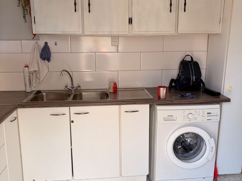 A functional laundry area featuring built-in white cabinetry, a stainless steel sink, tiled backsplash, and space for a front-loading washing machine.