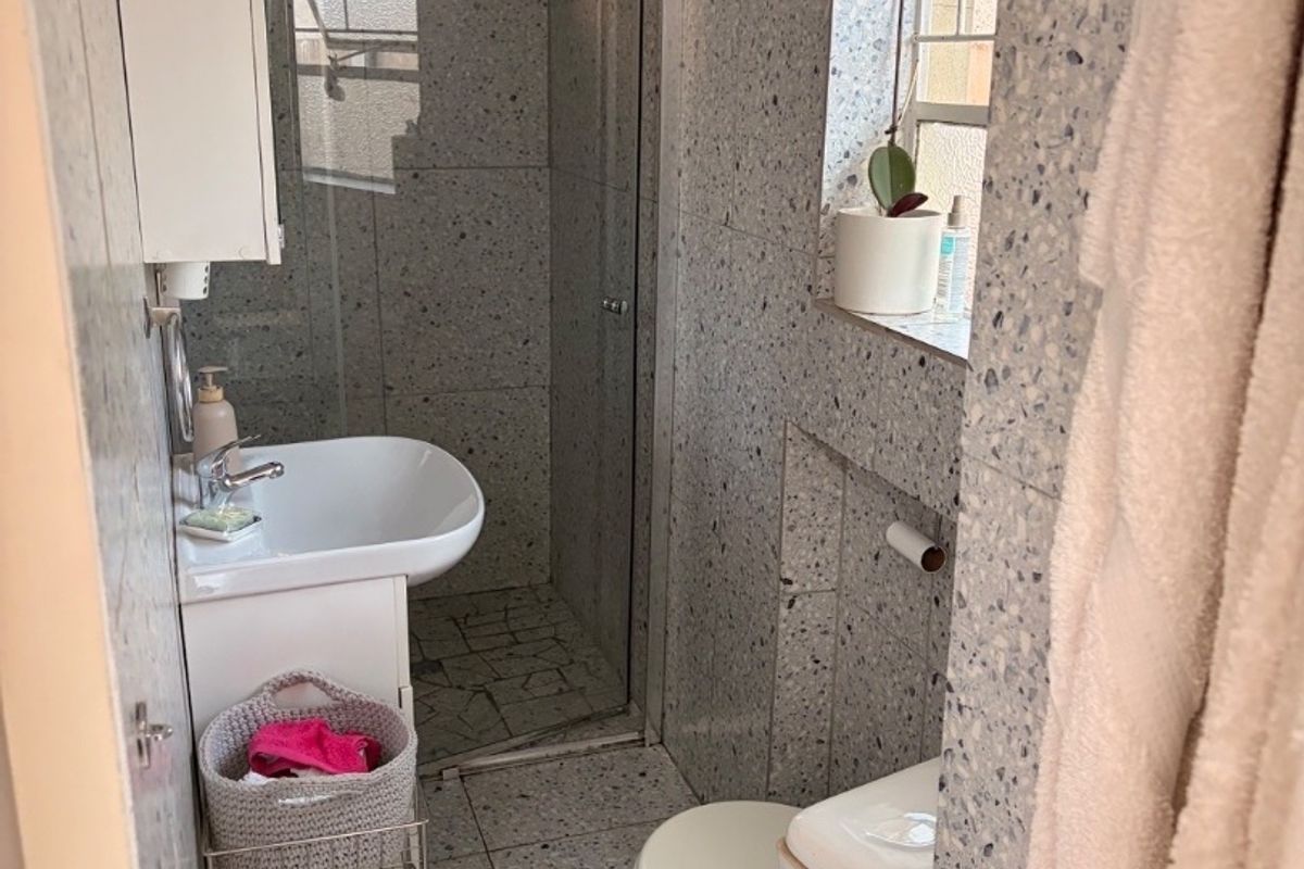 Compact bathroom featuring terrazzo-style wall and floor tiling, a glass-enclosed shower, a wall-mounted basin, and a standard toilet.