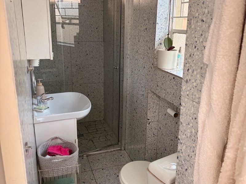 Compact bathroom featuring terrazzo-style wall and floor tiling, a glass-enclosed shower, a wall-mounted basin, and a standard toilet.