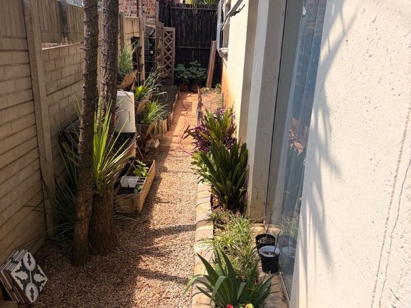 A narrow side garden path featuring gravel ground cover, bordered by a precast concrete fence and the exterior wall of the apartment.