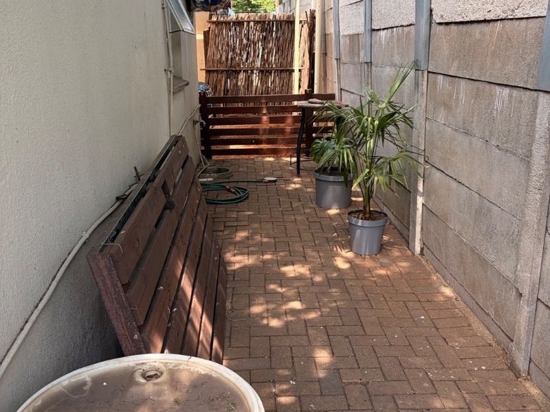 A narrow rear exterior walkway featuring paved flooring and a precast concrete boundary wall, offering potential for landscaping or outdoor storage improvement.