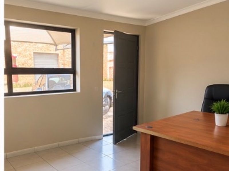 A functional office space featuring tiled flooring, neutral wall tones, and direct access to the exterior through a solid door.