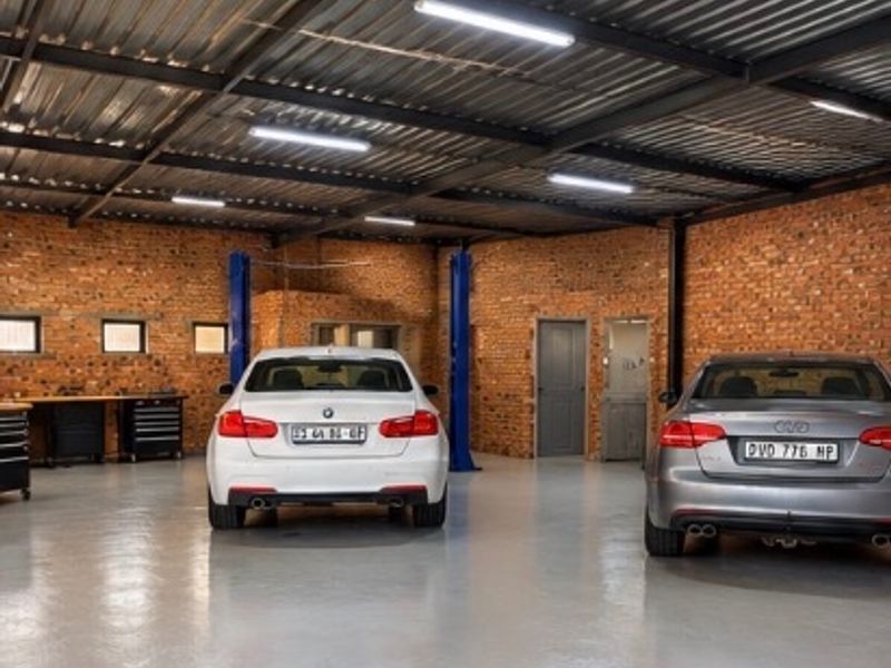 Spacious commercial garage featuring exposed brick walls, high-clearance corrugated metal ceiling, durable epoxy flooring, and integrated vehicle service lifts.