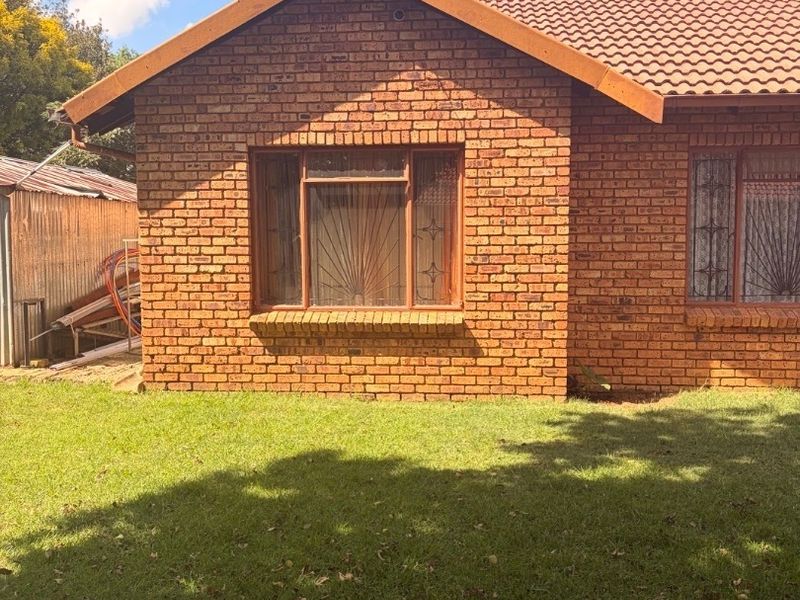 Rear view of a face brick house featuring a tiled roof, security bars on windows, and a surrounding lawn area.