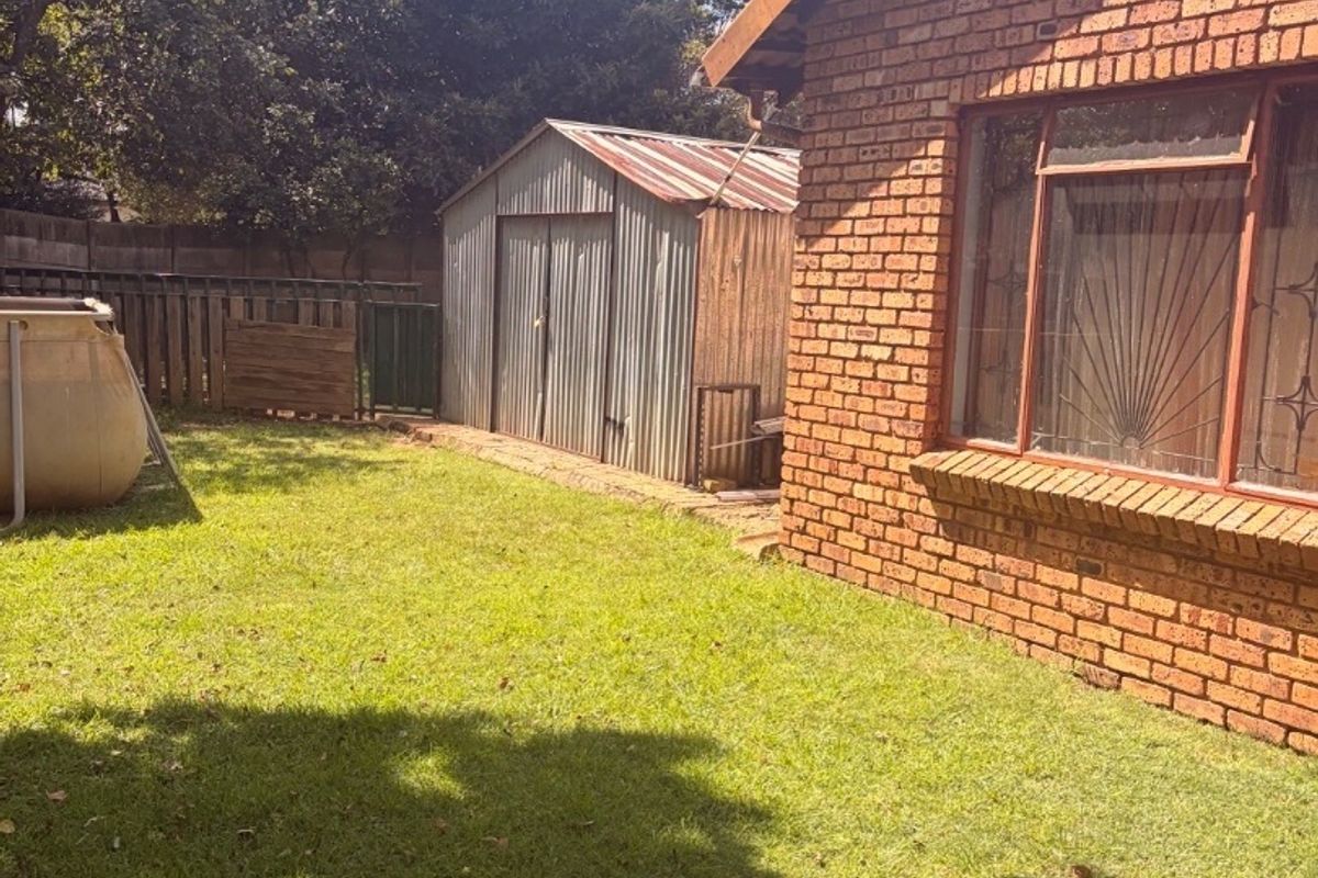 Rear garden view featuring a face brick house exterior, security-barred windows, and a detached metal storage shed set within a lawned backyard.