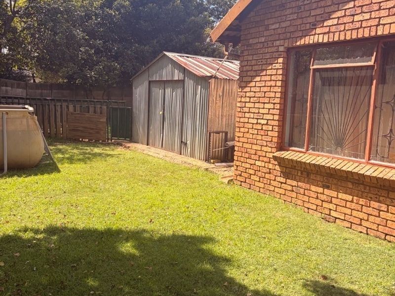 Rear garden view featuring a face brick house exterior, security-barred windows, and a detached metal storage shed set within a lawned backyard.