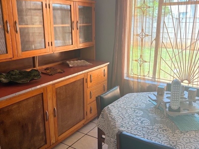 A dining area featuring tiled flooring and a window with a security gate, providing natural light and a view of the garden.