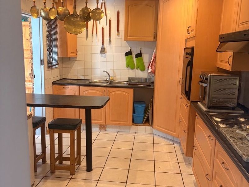 A functional kitchen featuring light wood cabinetry, tiled flooring, and built-in appliances, offering a practical layout with a breakfast bar area.