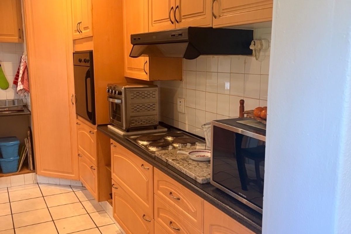 A functional kitchen featuring light wood cabinetry, stone countertops, tiled backsplash, and built-in appliances including an oven and hob.