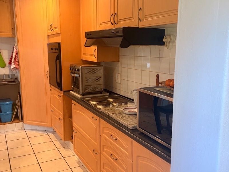 A functional kitchen featuring light wood cabinetry, stone countertops, tiled backsplash, and built-in appliances including an oven and hob.
