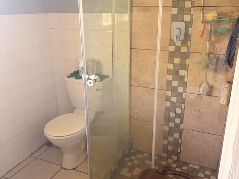 A functional bathroom featuring a glass-enclosed shower, toilet, and neutral tiled finishes throughout.