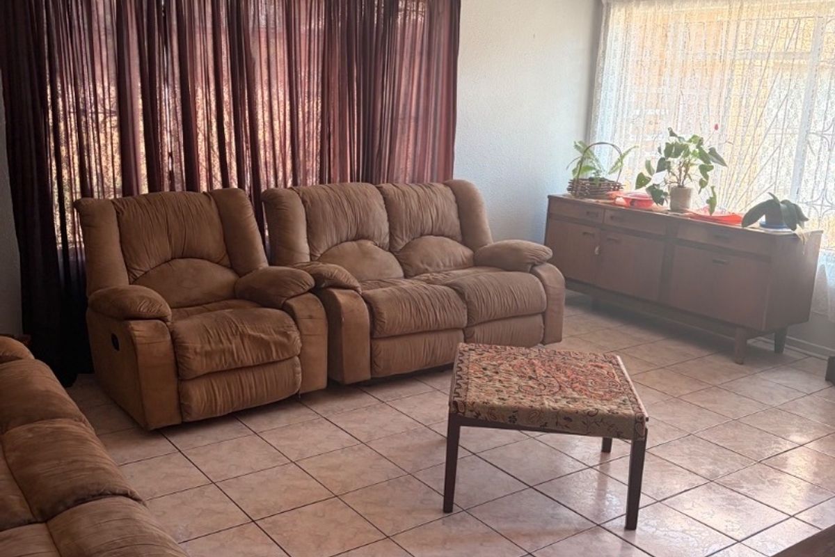 A spacious living room featuring neutral tiled flooring and recessed ceiling lighting, offering a functional layout with ample natural light.