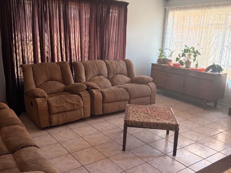 A spacious living room featuring neutral tiled flooring and recessed ceiling lighting, offering a functional layout with ample natural light.