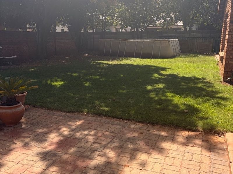 A private rear garden featuring a paved patio area, established lawn, and brick boundary walling, providing a functional outdoor space.