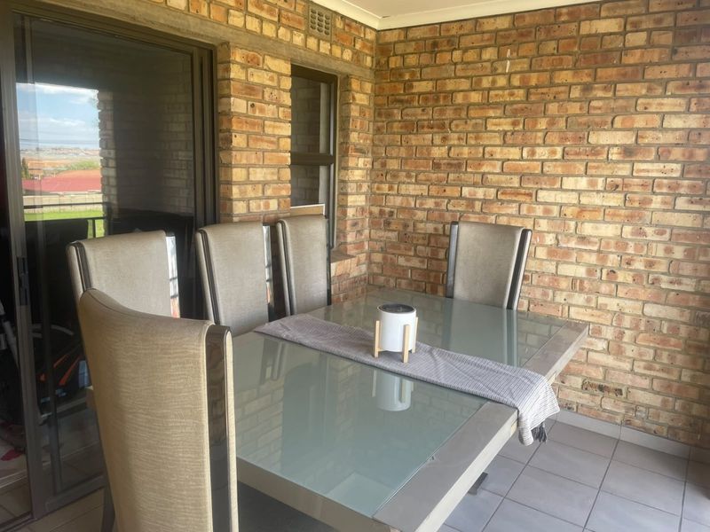 A covered patio area featuring exposed brick walls, tiled flooring, and a sliding glass door providing access to the interior.