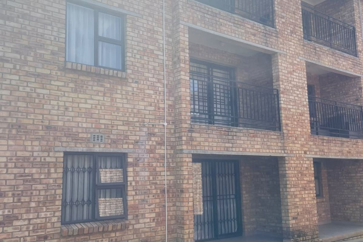 Exterior view of a multi-story apartment building featuring face brick construction, private balconies with security railings, and ground-level access points.