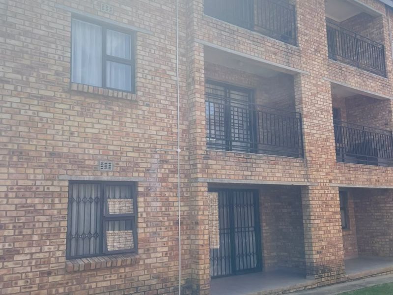 Exterior view of a multi-story apartment building featuring face brick construction, private balconies with security railings, and ground-level access points.