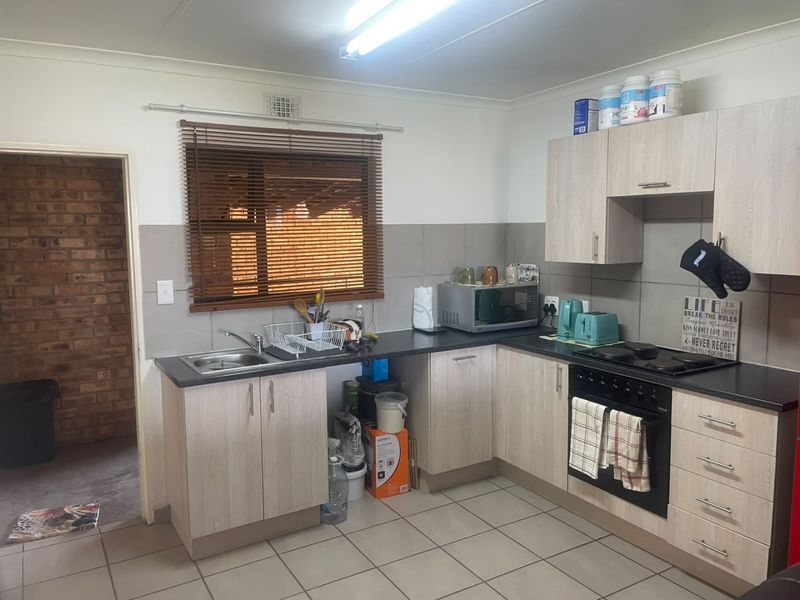 A functional kitchen featuring light wood-look cabinetry, dark countertops, a built-in oven and hob, tiled backsplash, and neutral floor tiles.