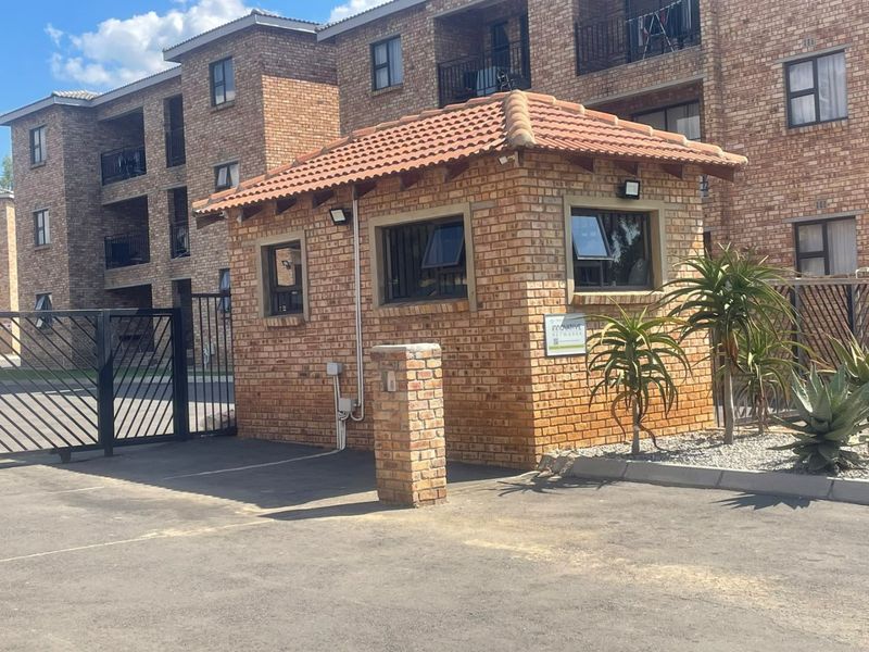A well-maintained face brick security guard house located at the entrance of the apartment complex, featuring a tiled roof and secure access gate.