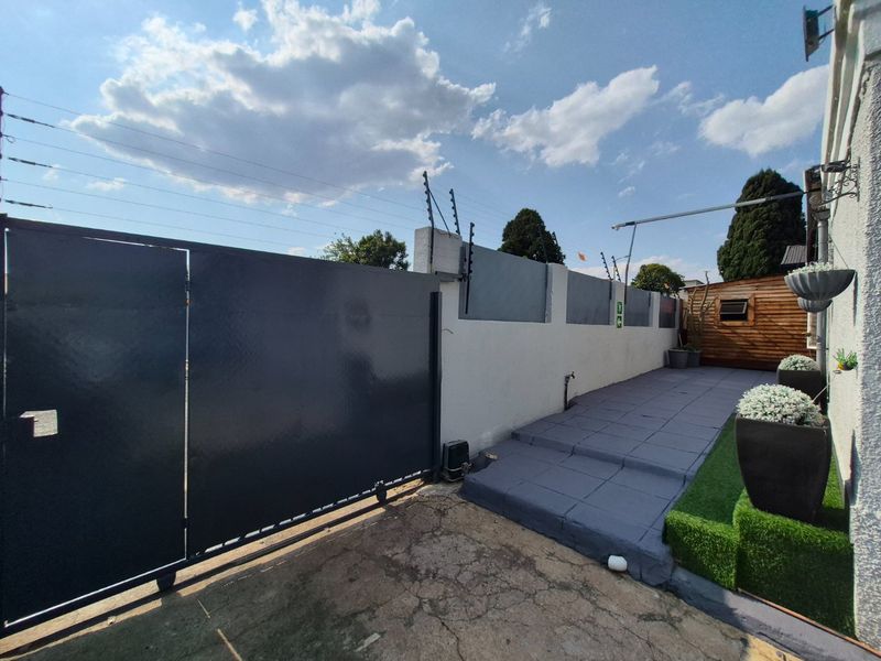 Front entrance area featuring a modern sliding gate, secure boundary wall with electric fencing, and a paved walkway leading to the property.