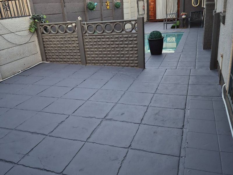 A paved outdoor patio area featuring a swimming pool, enclosed by boundary walls with integrated electric fencing.