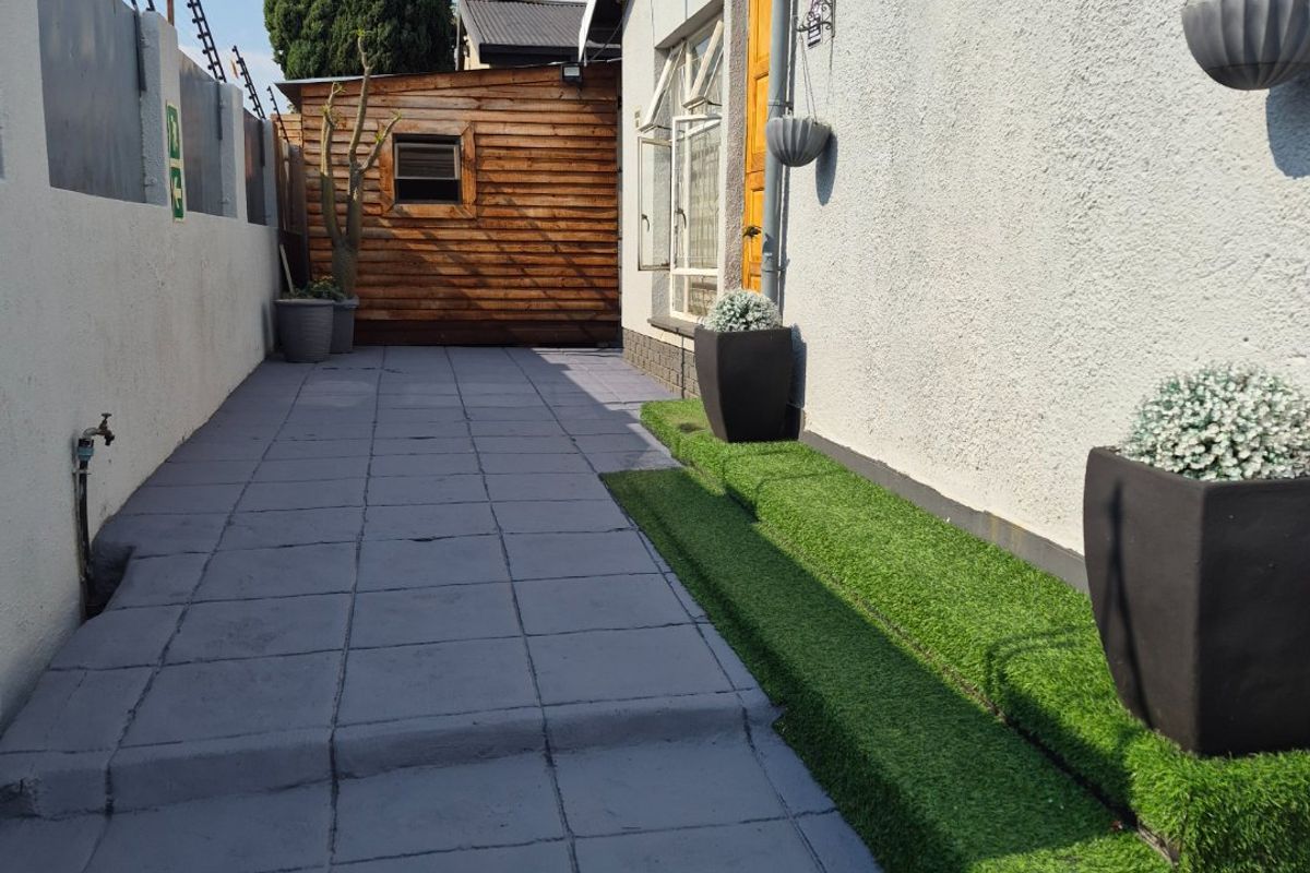 A well-maintained rear exterior area featuring a paved walkway, artificial grass steps, and a timber storage shed along the boundary wall.