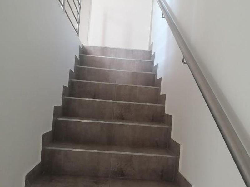A clean, modern staircase featuring tiled steps, a sleek metal handrail, and a matching metal balustrade leading to the upper level.