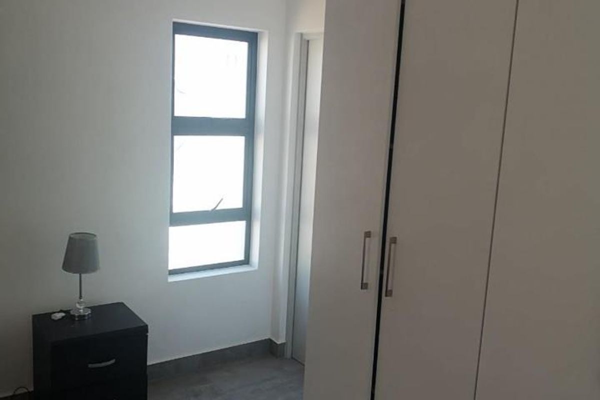 A clean, modern bedroom featuring neutral tiled flooring, a large built-in wardrobe, and crisp white walls, offering a bright and functional living space.