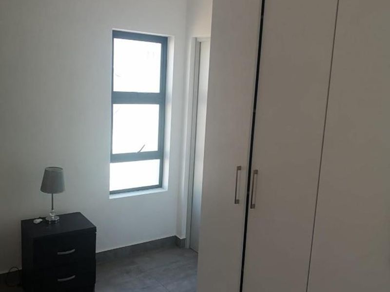 A clean, modern bedroom featuring neutral tiled flooring, a large built-in wardrobe, and crisp white walls, offering a bright and functional living space.