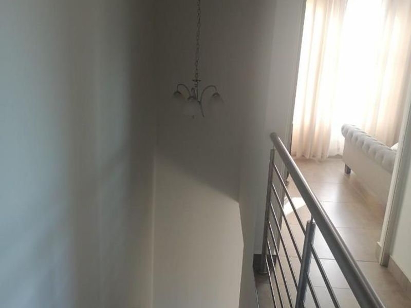 A staircase area featuring a modern stainless steel balustrade, wall-mounted handrail, and a pendant light fixture, leading to an adjacent living space.