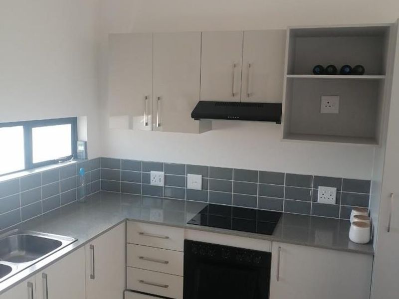 Modern kitchen featuring sleek white cabinetry, grey stone countertops, subway tile backsplash, and integrated appliances including an electric hob and oven.