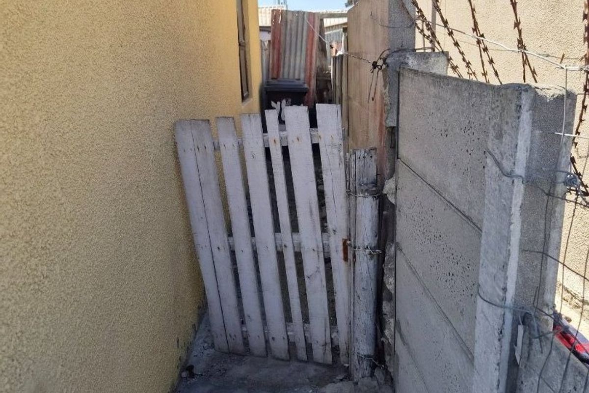 A narrow side passage featuring a precast concrete boundary wall with barbed wire and a weathered wooden gate.