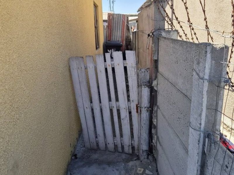 A narrow side passage featuring a precast concrete boundary wall with barbed wire and a weathered wooden gate.